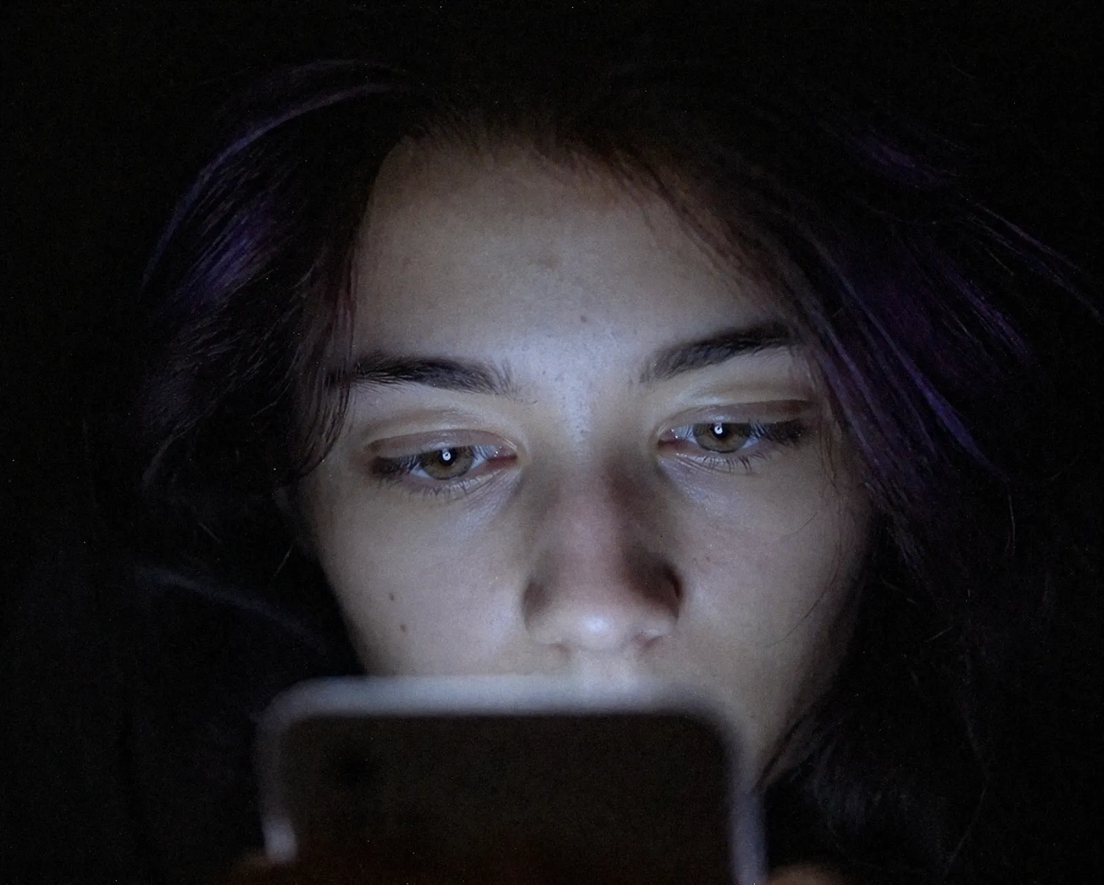 gen-z-phone-isolation Young woman staring into mobile phone with emotionally flattened expression during modern civilian activity.
